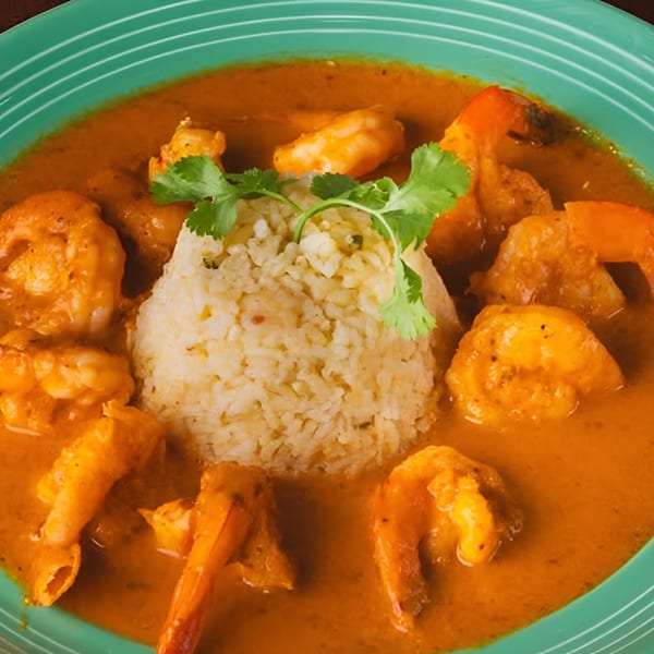 Shrimp in a rich orange sauce with a mound of rice and cilantro on a green plate.
