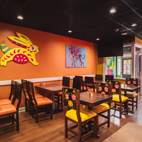 Colorful Los Alebrijes Mexican Restaurant dining room with vibrant orange walls and decorative chairs.