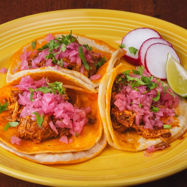 Three Los Alebrijes Mexican Restaurant tacos with meat, pickled onions, cilantro, radishes, and lime.