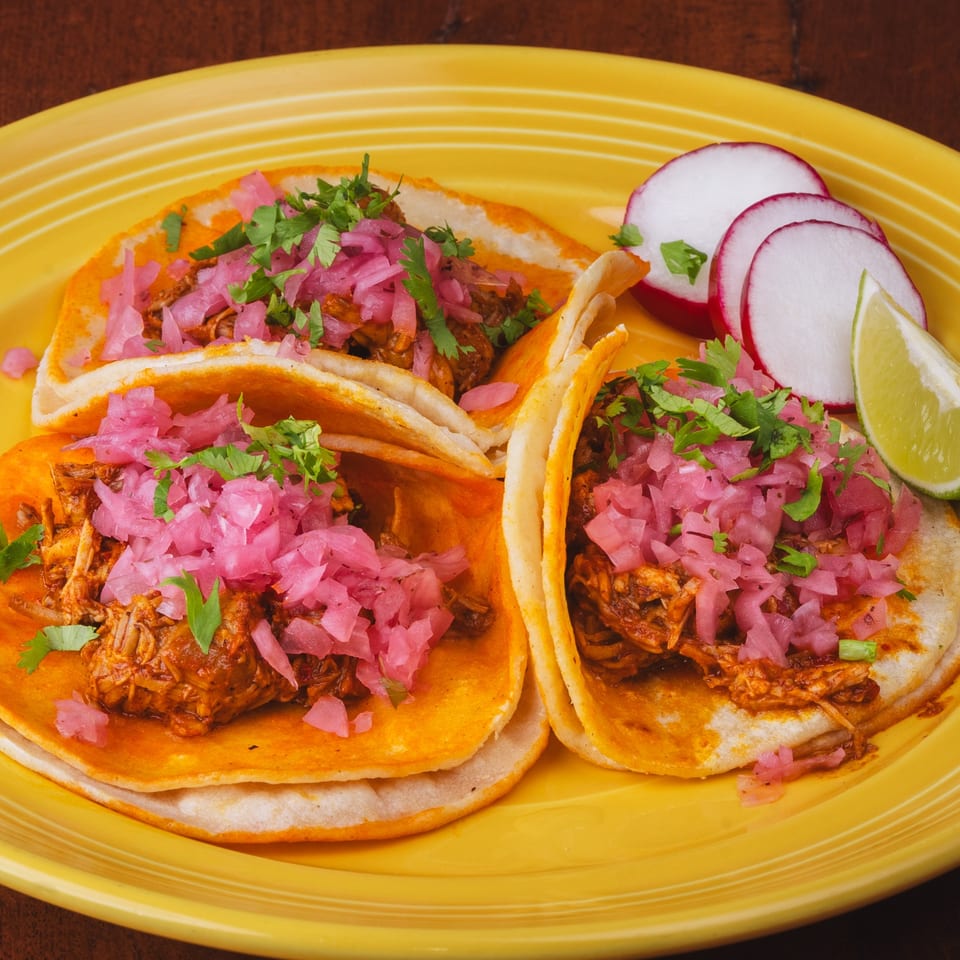 Three Los Alebrijes Mexican Restaurant tacos with meat, pickled onions, cilantro, radishes, and lime.