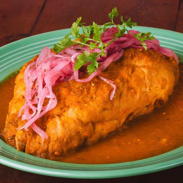A large, saucy Mexican burrito topped with pickled red onions and fresh cilantro on a green plate.
