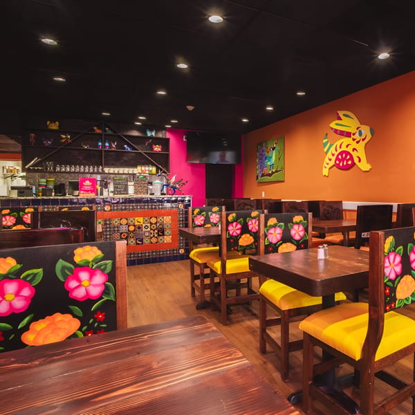 Vibrant interior of Los Alebrijes Mexican Restaurant with colorful decor, floral chairs, and a bar area.