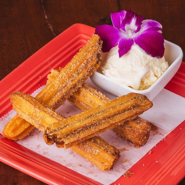 Golden churros dusted with sugar and cinnamon, served with vanilla ice cream and a purple orchid.