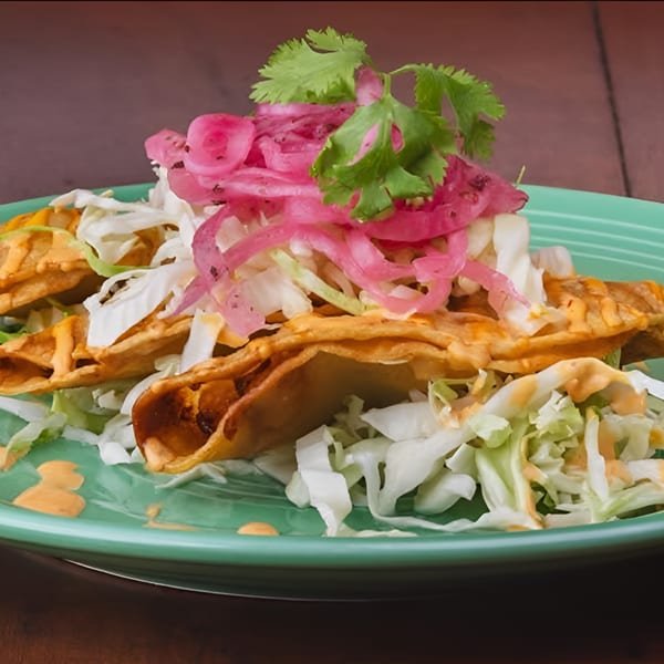 Crispy taquitos topped with shredded lettuce, pickled red onions, cilantro, and a creamy sauce.